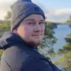 Migreeniyhdistyksen hanketyöntekijä Matti Mannonen hymyilee. Kasvokuva. Taustalla puita ja aurinko paistaa.